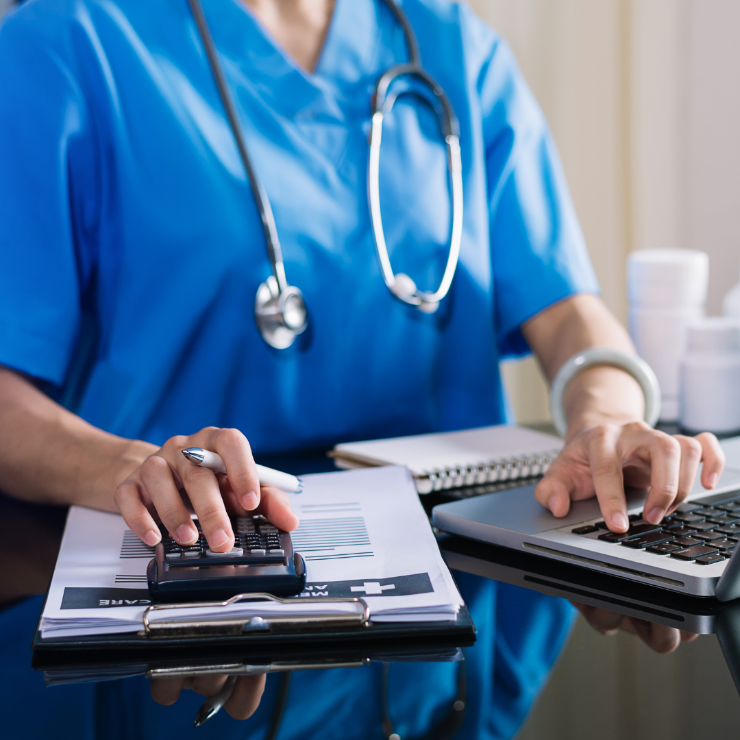 Doctor working on computer while also using calculator and notepad.